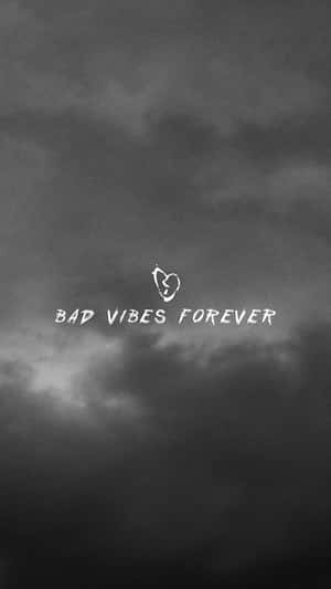 黑暗多雲的天空，有白色文字寫著bad vibes forever和一個破碎的心形符號。