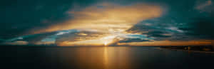 海面上日落，金色光芒穿透黑暗的雲層。