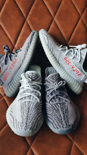 灰色針織Yeezy運動鞋，帶有紅色文字，置於棕色絎縫皮革上。 — iPhone 7 壁紙