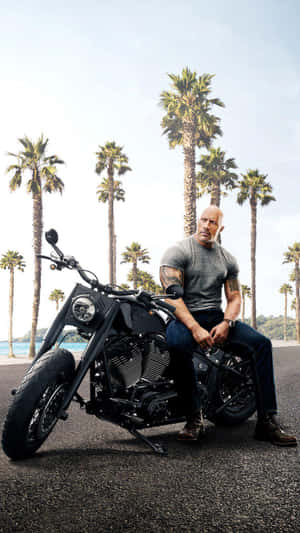 Dwayne Johnson 坐在一輛黑色電單車上，背景有棕櫚樹。