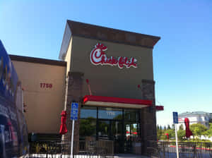 Chick-fil-A 餐廳外觀，有紅色遮陽篷和關閉的庭院傘，在晴朗藍天下。
