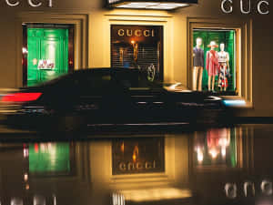 黑色汽車在夜間駛過Gucci商店，霓虹綠色窗戶和金色招牌映照在濕漉漉的人行道上。