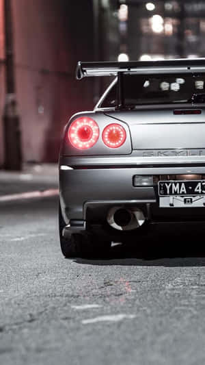 銀色日產Skyline GT-R，紅色尾燈，夜晚潮濕城市街道。