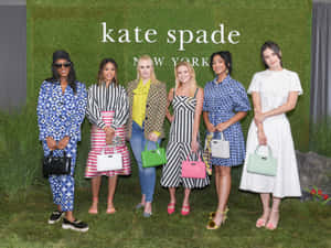 六位穿著時尚服裝和手袋的女性在草地上參加 Kate Spade 活動時擺姿勢。