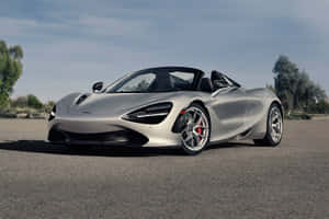 銀色McLaren 720S Spider開篷跑車停在鋪砌的道路上，有樹木和天空。