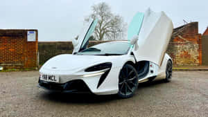 白色McLaren跑車，鷗翼門打開，停在磚牆附近的碎石地上。