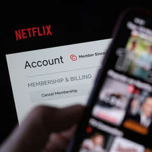 手拿著帶有Netflix應用程式的手機，而筆記本電腦顯示帳戶帳單選項。
