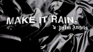 皺褶黑色緞面布料上的粗體白色文字寫著 make it rain palm angels。