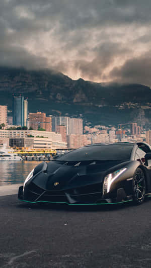 黑色林寶堅尼 Veneno 停在水邊，背景是摩納哥城市和山脈，天空風起雲湧。