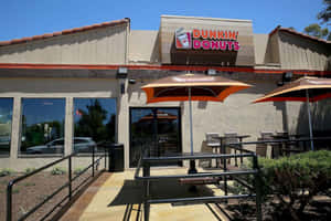 晴朗日子裡，橙色遮陽傘下設有戶外座位的 Dunkin' Donuts 咖啡店。 — 早晨咖啡 壁紙