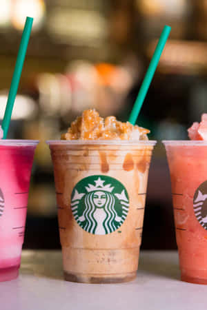 三杯Starbucks冰飲，配有綠色吸管和焦糖配料，放在櫃檯上。