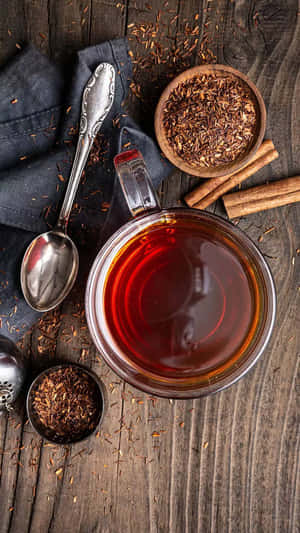 一杯博士茶玻璃杯，配以肉桂棒和散裝茶葉，放在木桌上。 — 青綠色 GIF 壁紙