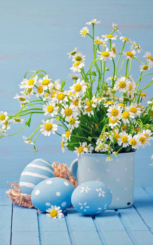 木桌上馬克杯中的裝飾性藍色復活節彩蛋和雛菊。 — Moto Pad 壁紙