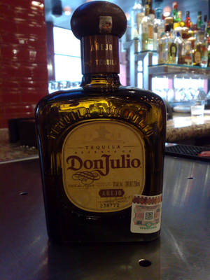 一瓶Don Julio Añejo龍舌蘭酒在酒吧，後面有紅磚牆和架子。