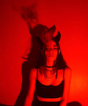 女人戴著惡魔角和頸鏈，身後紅光中煙霧升騰。