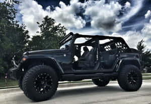 黑色Jeep Wrangler車門打開，停在有樹木和多雲天空的車道上。