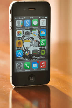 木桌上的白色iPhone 4s，顯示主屏幕，帶有應用程式圖標和87%電量。