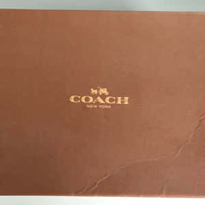 棕色 Coach New York 品牌盒子，帶有金色標誌和可見摺痕。