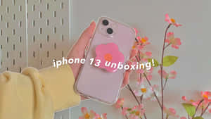 手拿著粉紅色iPhone 13，帶花朵彈出式插座，靠近粉彩花朵。