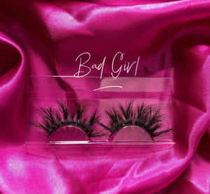 透明盒中的黑色假睫毛，置於粉紅色緞面上，帶有「Bad Girl」文字。