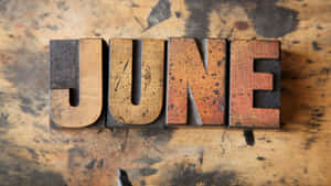 復古木製活字塊在污漬木面上拼出JUNE。 — 夏日氣息 壁紙