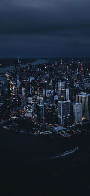 密集城市的夜間鳥瞰圖，有明亮的建築物和黑暗的水面。 — Galaxy A15 壁紙
