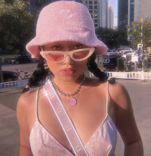 年輕女性戴著粉紅色漁夫帽和太陽眼鏡，在日落時分的城市人行道上。