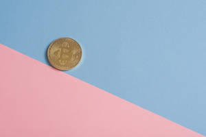 金色比特幣硬幣在粉紅色和藍色背景上。