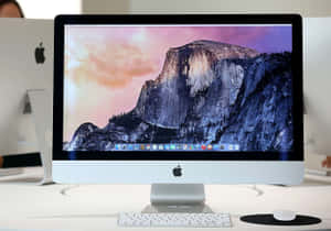 銀色 iMac 在白色桌子上顯示 Half Dome 日落壁紙，配有鍵盤和滑鼠。