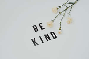 黑色字母拼出「BE KIND」，與淡奶油色康乃馨一同置於白色表面上。