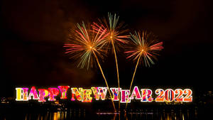 煙火在水面上綻放，'Happy New Year 2022' 以彩色字母閃耀。