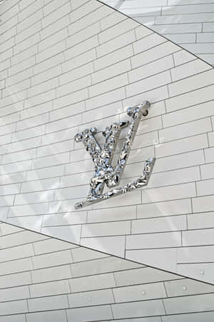白色瓷磚建築外牆上的鉻色 Louis Vuitton 標誌，帶有幾何線條。 — 路易威登 壁紙