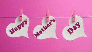 三個心形卡片，上面有「Happy Mother's Day」文字，夾在鐵絲上，背景為粉紅色。