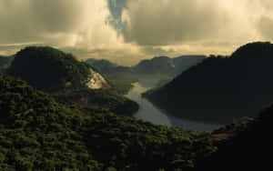 一條河流流經茂密的青山，天空多雲，帶有金色光芒。