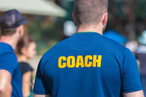 男士身穿藍色襯衫，印有黃色COACH文字，在戶外陽光下。