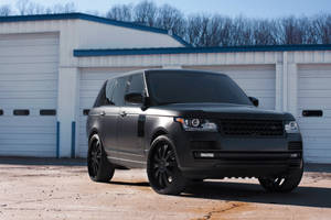 霧黑色Range Rover Sport停泊在白色工業建築前。