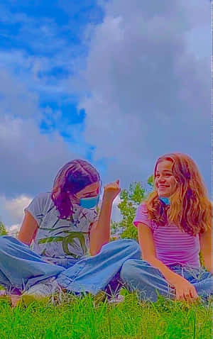 兩個微笑的女孩坐在草地上，戴著口罩，在藍天白雲下。