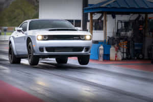 銀色Dodge Challenger SRT在潮濕的直線加速賽道上加速，背景有車庫。