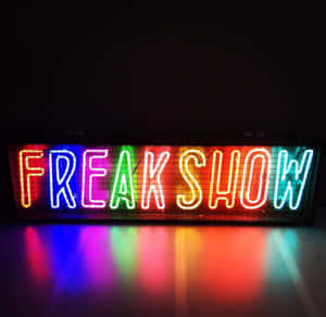 一個色彩繽紛的霓虹燈牌，上面寫著 freak show，彩虹燈光在黑暗表面上反射。