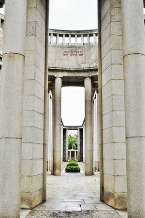 帶有柱子和刻字的石製紀念拱門，通往花園。 — 低飽和度 壁紙