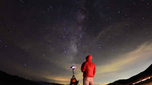 穿著紅色外套的人夜晚站在山上觀看星星和銀河。