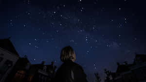 人站在外面仰望房屋上方的繁星夜空。 — 星星 壁紙
