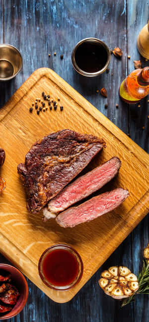 切片 medium-rare 牛排，配大蒜、迷迭香和醬汁，置於木板上。 — 三星 Galaxy S20 壁紙