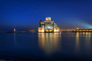 夜晚發光的現代博物館，帶有水影和城市燈光。 — 藍色美學 壁紙