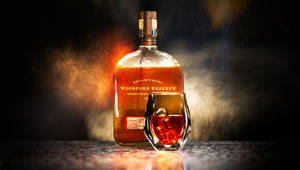 Woodford Reserve 波本威士忌瓶和帶冰塊的玻璃杯在酒吧上，有煙霧和溫暖的燈光。