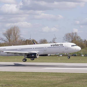 Volaris飛機在跑道上，背景有風力渦輪機和樹木