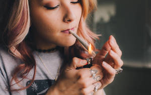 年輕粉紅髮女性在室內點燃大麻煙。