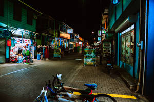 夜間街道，有商店和停放在鋪砌人行道上的自行車。 — 3:2 壁紙