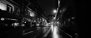 一個人在夜晚獨自走在濕漉漉的城市街道上，路燈下。 — 夜景城市 壁紙