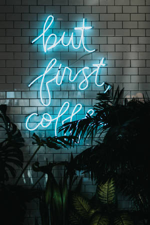 藍色霓虹燈牌寫著 but first coffee，背景是帶植物的瓷磚牆。